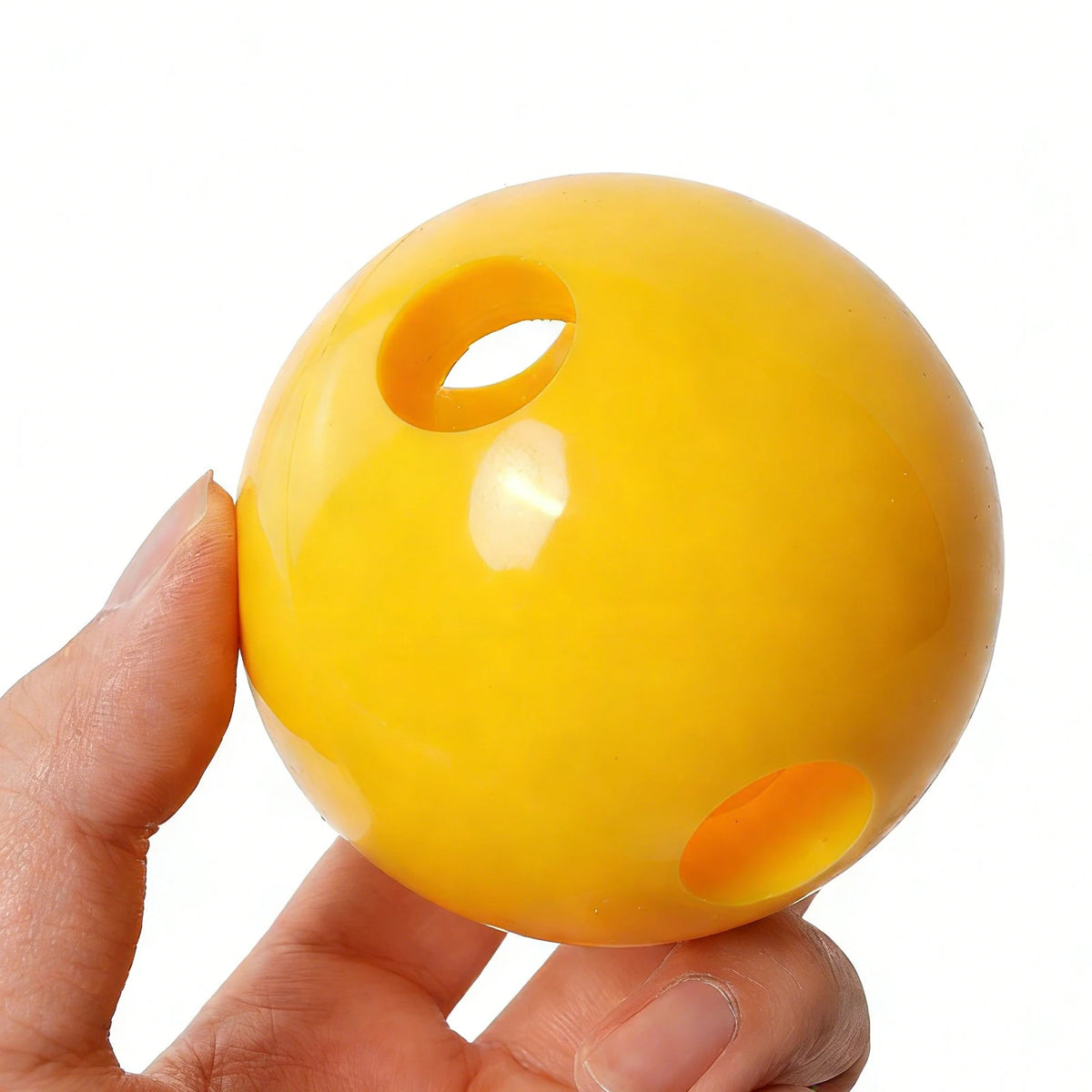 Yellow PVC training ball held by fingers, showing top and side holes