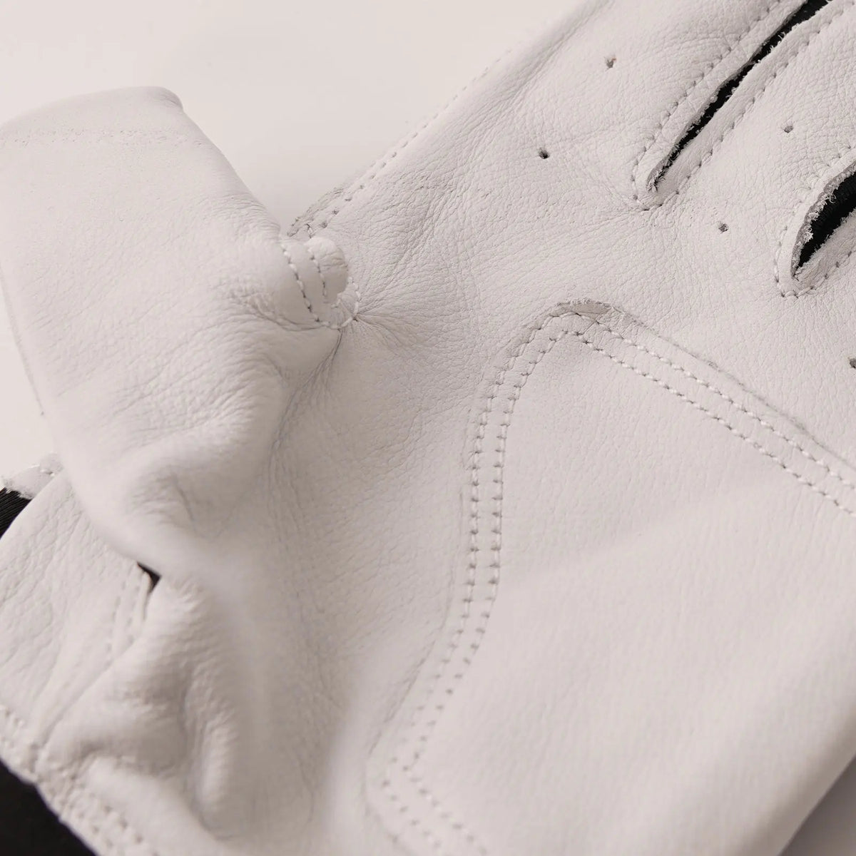 White leather batting glove close-up with stitched grip panel and perforations